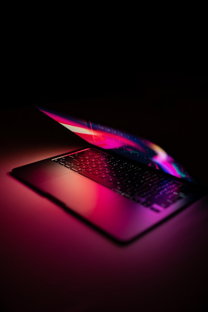 Stylish laptop with neon reflections, partially open, on a dark setting.